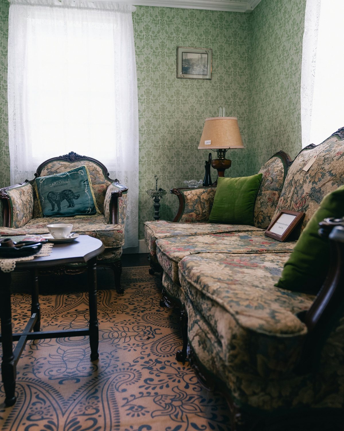 Traditional sitting room with pale green patterned wallpaper, floral sofas and a patterned tiled floor