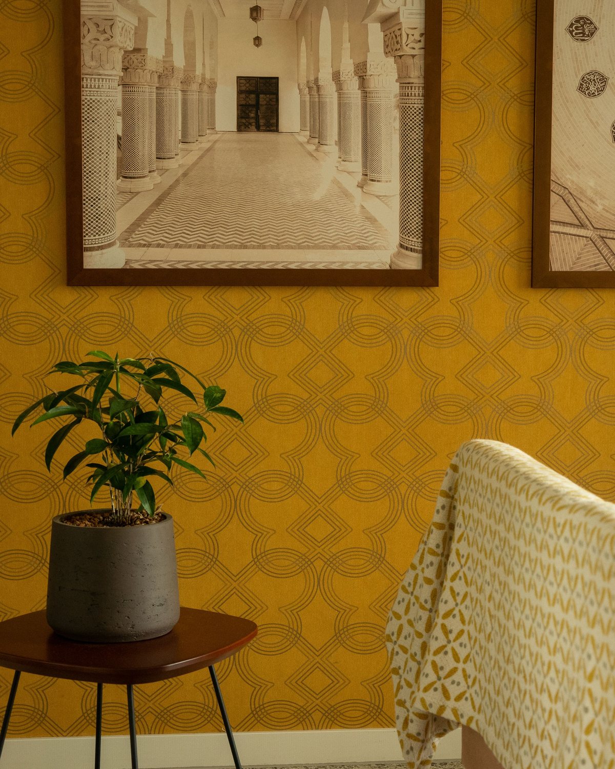 Mustard wallpaper with a subtle lattice pattern, a framed architectural photograph and a potted plant on a side table