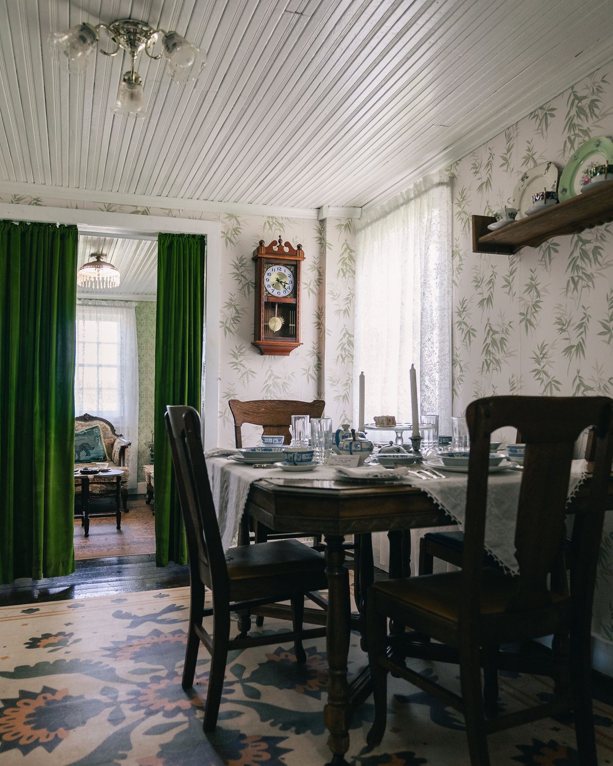 Dining room with delicate botanical wallpaper, deep green curtains, a pendant light and a dressed dining table