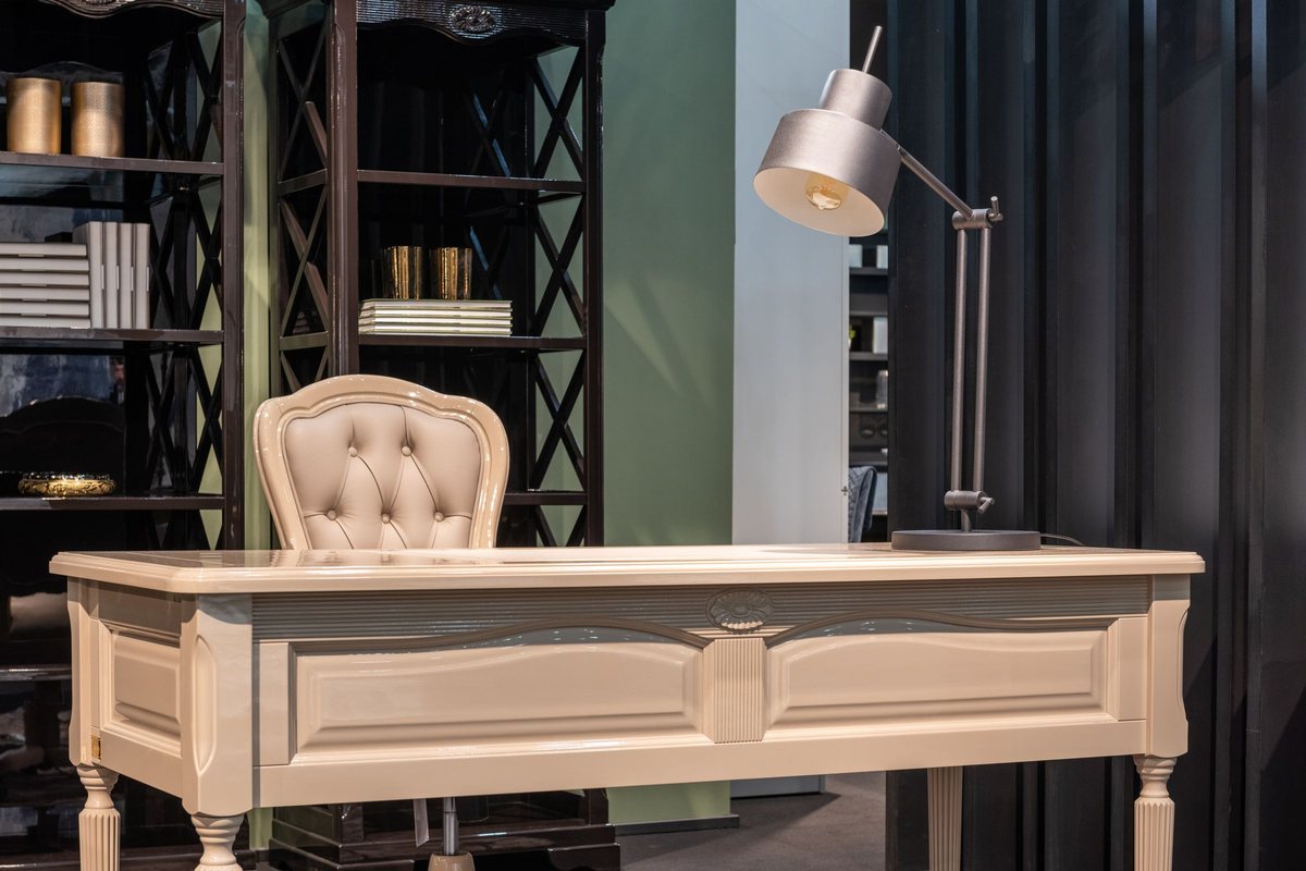 Home study with a deep green wall, dark built-in shelving, a pale writing desk and a task lamp