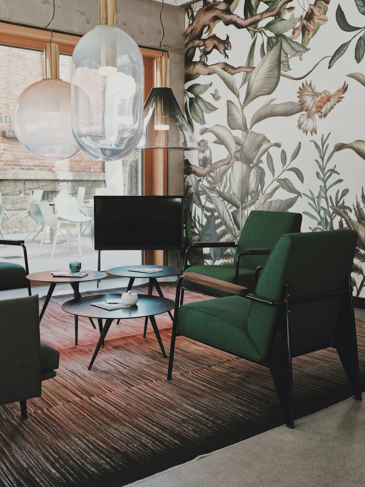 Sitting area with a botanical mural wallpaper of birds and foliage, dark green armchairs and glass pendant lights