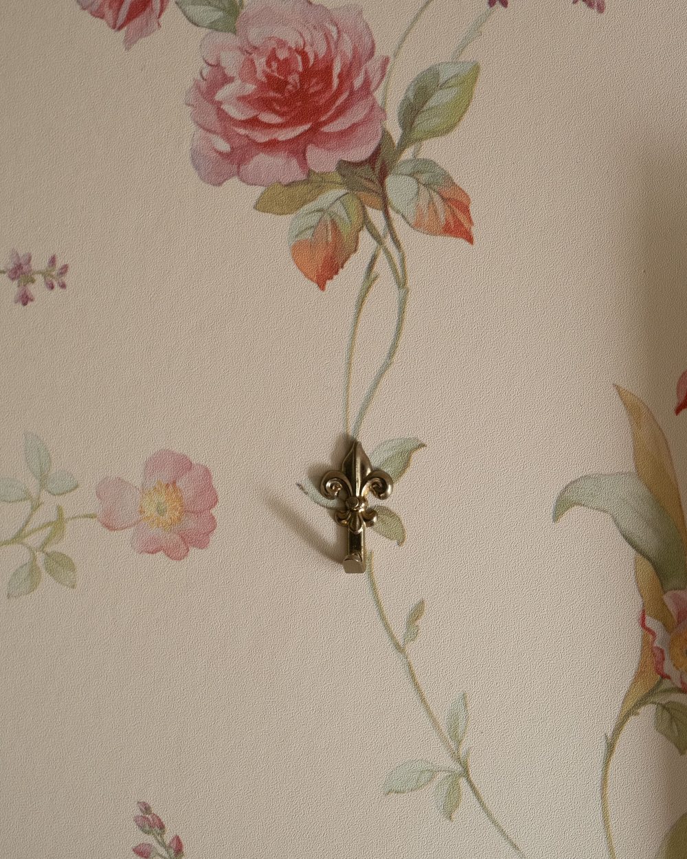 Close view of soft floral wallpaper with a small brass wall hook, showing the paper lying flat against the wall